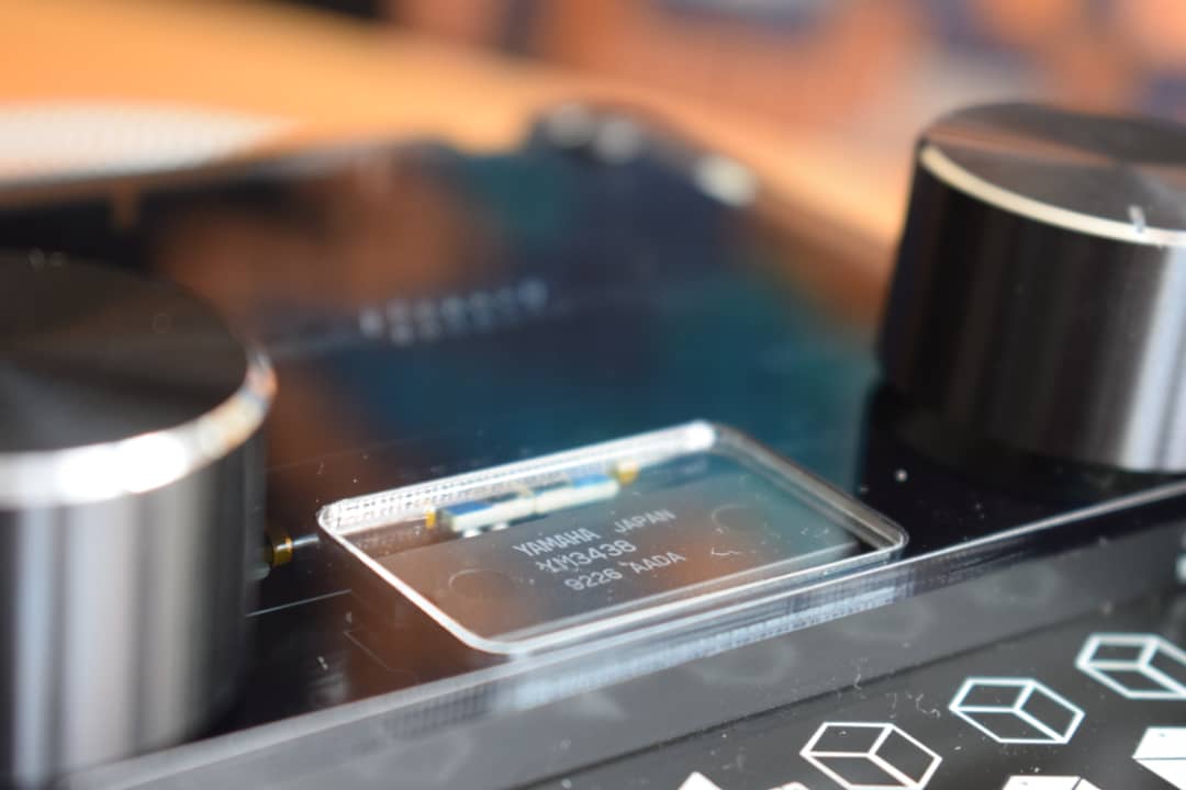 Close-up of a genuine Yamaha YM3438 chip under the clear acrylic window of a DAFM synth GENESIS, between its two aluminium knobs