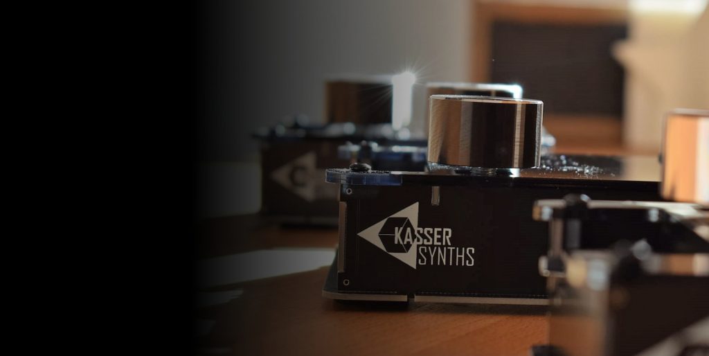 Black DAFM synth case with the Kasser Synths logo and a silver knob on a wooden table